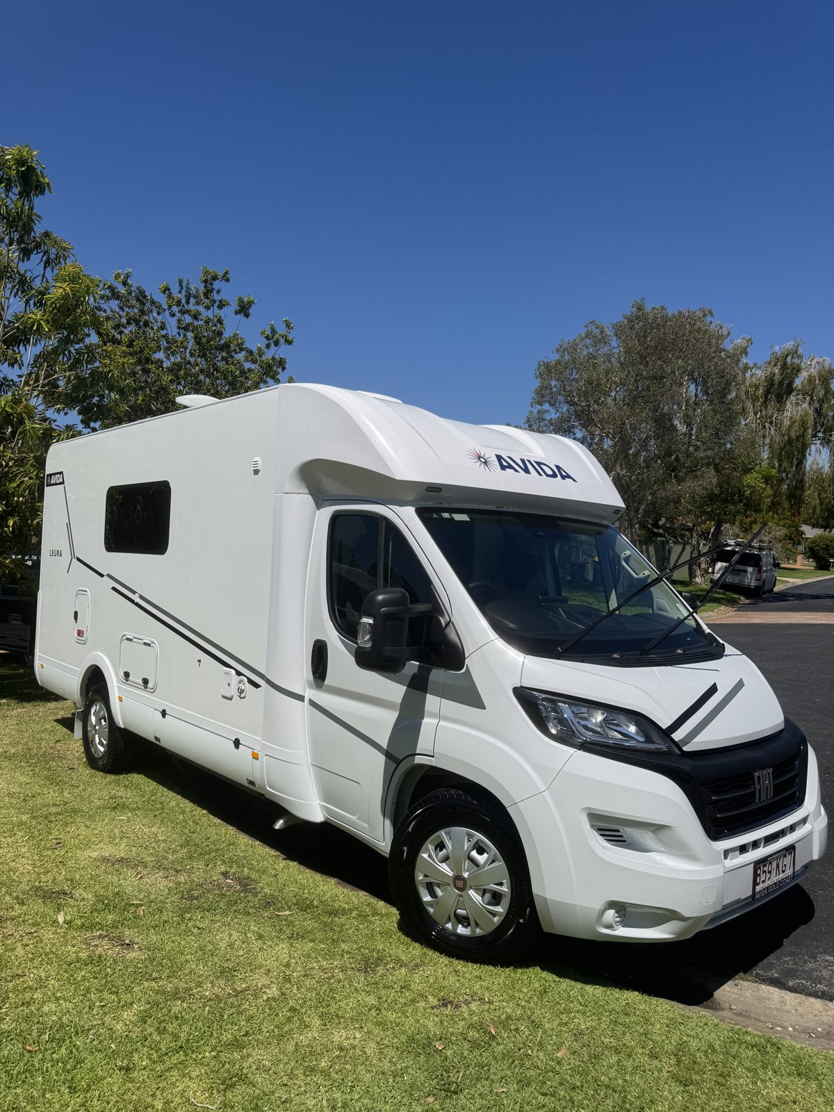 A white Avida motorhome parked on grass, photographed side-on in daylight